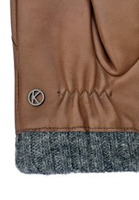 Brown leather glove with gray knitted cuff, featuring a stitched detail and a circular logo at the wrist. Texture appears smooth and soft.