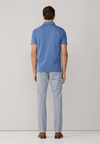 Polo bleu à manches courtes avec col, associé à un pantalon bleu clair. Chaussures marron visibles en bas. Couleurs simples et unies.