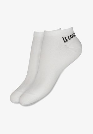 Calcetines tobilleros blancos hechos de una mezcla de algodón, con una textura suave y puños acanalados, y el logo "Le Coq Sportif" en negro.