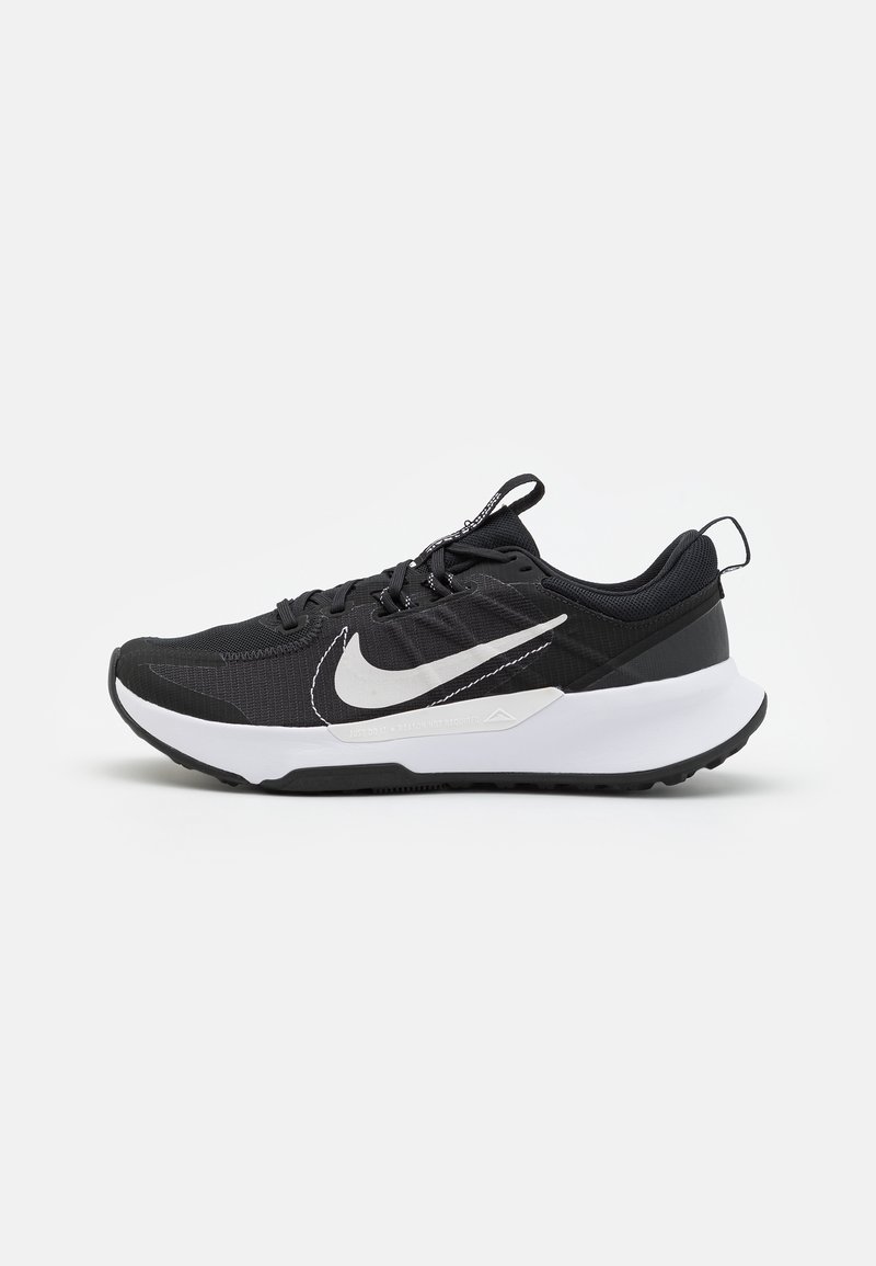 Zapatilla deportiva negra con una parte superior de malla texturizada, entresuela blanca, suela de goma y un destacado logo de swoosh blanco en el lateral.
