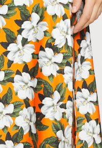 Robe fleurie présentant des fleurs de magnolia blanc sur un fond orange, avec des feuilles vertes, des détails cousus et une texture de tissu raffinée.