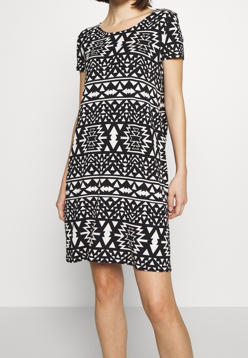 Robe à manches courtes en tissu doux et extensible, présentant un motif géométrique noir et blanc avec des formes triangulaires et étoilées.