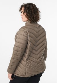 Pruhovaná pufovaná bunda v khaki farbe so vzorom chevron, vysokým golierom a elastickými lemami. Textúrovaná, ľahká tkanina poskytuje izoláciu.