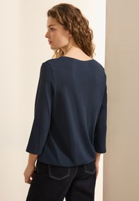 Dunkelblaues Langarmshirt mit Rundhalsausschnitt und glatter Textur, getragen mit dunklen Hosen. Die Sicht ist von hinten und zeigt Details an den Schultern.