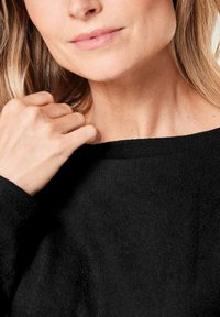 Schwarzer Strickpullover mit weitem Ausschnitt. Weiche Textur und lockere Passform, teilweise zu sehen mit einer Hand, die den Stoff an der Schulter greift.