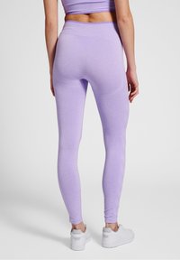 Jasnofioletowe legginsy o gładkiej fakturze, wysokim pasie i dopasowanym kroju, w połączeniu z białymi butami sportowymi.