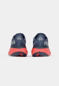 Baskets de course bleu et gris avec une tige en maille texturée et une semelle intermédiaire corail. Présente un logo HOKA et une semelle extérieure crantée pour une meilleure adhérence.