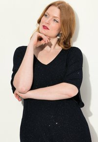 Haut noir scintillant avec un décolleté en V et des manches courtes. Le tissu a une apparence texturée et pailletée, créant un effet de brillance subtil.