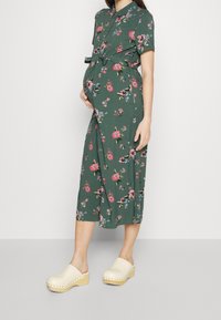 Abito da maternità floreale, verde, al ginocchio, con maniche corte e vita regolabile con nastro. Abbina a zoccoli in legno chiaro con punta rotonda.