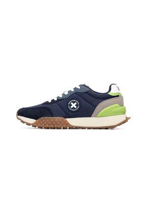 Zapatilla deportiva en azul marino y verde con parte superior texturizada, logo redondo, cordones blancos y suela de goma con puntos elevados para agarre y amortiguación.