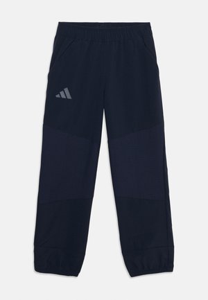 Pantalon de sport bleu marine avec taille et poignets élastiques, poches latérales, et un logo Adidas réfléchissant sur la cuisse gauche.