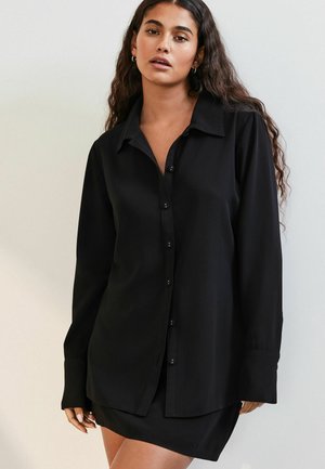 Zwart langemouwen shirt met een knoopsluiting aan de voorkant, met notch-kraag en een relaxte pasvorm, gecombineerd met een bijpassende zwarte minirok. Glad textuur.