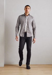 Muška košulja na dugih rukava sa geometrijskim uzorkom, u sivoj nijansi, uparena s crnim slim-fit hlačama i crnim kožnim cipelama.