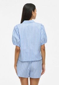 Top a maniche corte a righe blu e bianche con colletto, caratterizzato da maniche a palloncino e orlo dritto. Abbinato a pantaloni corti coordinati.