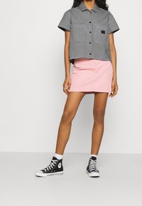 Camicia a maniche corte a quadretti bianco e nero, gonna di jeans rosa e sneaker alte nere con suole bianche. Design semplice, vestibilità casual.