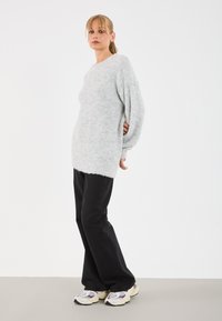 Pull en maille gris clair, à coupe décontractée et manches larges, associé à un jean noir à jambes larges et des baskets multicolores. Design simple.