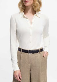 Ivory blouse met lange mouwen en een kraag, voorzien van een knoopsluiting. Gecombineerd met beige linnen broek en een geweven zwarte leren riem.