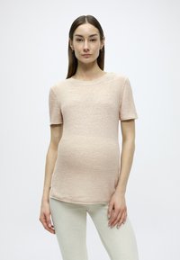 Haut tricoté rose pâle à manches courtes avec une finition texturée, encolure ronde, et un ourlet arrière légèrement plus long, associé à des leggings de couleur claire.