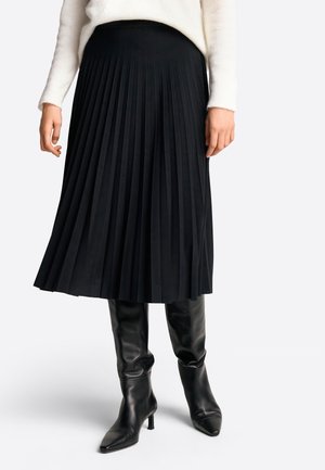 Svart plisserad kjol med ett slätt midjeband, i kombination med knähöga svarta skinnstövlar med spetsig tå och stilettklack.