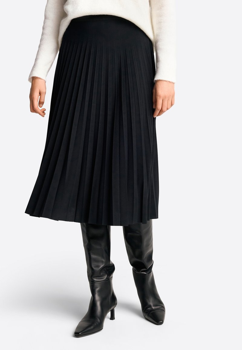 Czarna plisowana spódnica z gładką talią, w połączeniu z czarnymi skórzanymi kozakami do kolan z ostrym noskiem i szpilką.
