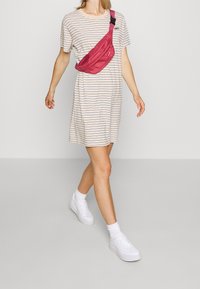 Pasiasta, beżowa sukienka z krótkimi rękawami, z granatowymi liniami. Slim, czerwony worek na ramię i białe trampki dopełniają casualowy wygląd.