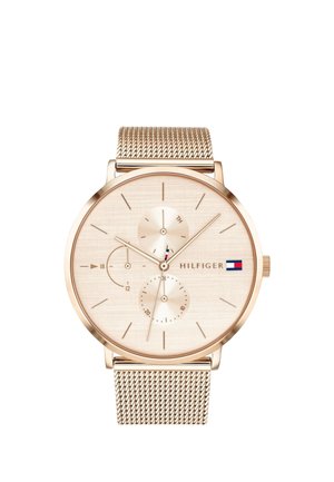 Reloj de pulsera analógico en tono dorado con correa de malla, esfera minimalista, dos subesferas y logotipo de Tommy Hilfiger con bandera roja, blanca y azul.