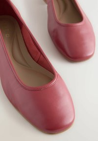 Bailarinas de cuero rojo con punta redondeada, textura suave y un perfil bajo. El forro interior es beige y presenta detalles de costura mínimos.