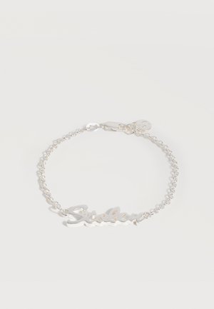 Srebrna bransoletka z łańcuszkiem, ozdobioną imienną tabliczką "Sisley" pisaną kursywą oraz małym okrągłym zawieszkiem blisko zapięcia na białym tle.