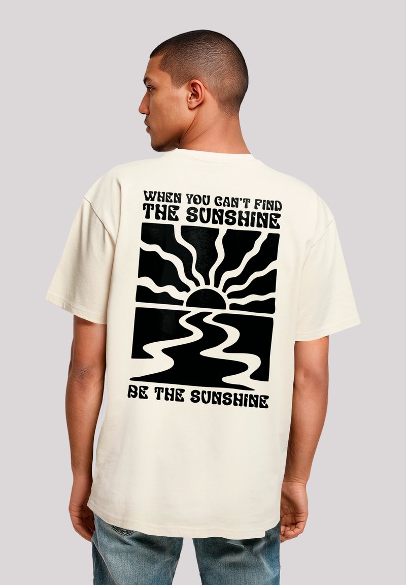 Beige cotton t-shirt with a back graphic: black sun rays above a wavy river and text "When you can't find the sunshine, be the sunshine."