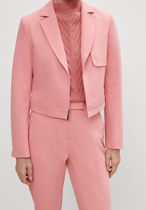 Femme portant une tenue rose coordonnée avec un blazer court, un pantalon taille haute et un pull en maille texturée.