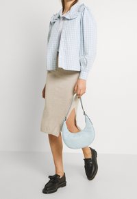 Světle modrá kostkovaná halenka s nabíranými rukávy, béžová sukně po kolena s bočním rozparkem, černé boty a světle modrá kabelka.