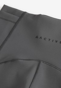 Leggings activewear neri con una texture liscia, caratterizzati da cuciture piatte e un logo sulla vita. Il materiale sembra elastico e aderente.