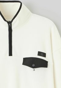 Pull-over en polaire blanche à demi-zip avec un col noir. Il dispose d'une poche poitrine avec rabat et bouton, agrémentée d'un patch logo noir.