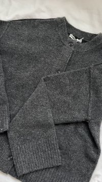 Szürke kardigán puha anyagból, zárt kialakítással, két gombbal, bordás mandzsettákkal és texturált felülettel.