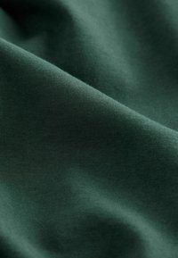 Dunkelgrüner Stoff mit glatter Textur und subtiler Glanzoberfläche, der eine Nahaufnahme des weichen, dehnbaren Materials zeigt.