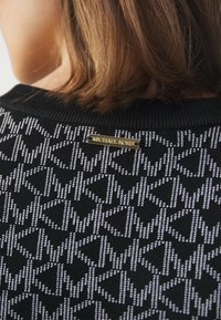 Maglione nero con motivo a stampa, caratterizzato da un design geometrico distintivo e una piastra con il logo dorato "Michael Kors" al collo. Texture in maglia morbida.