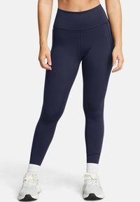 Marina höga leggings i ett elastiskt material, med platta sömmar och en kroppsnära passform, tillsammans med ljusa träningsskor.