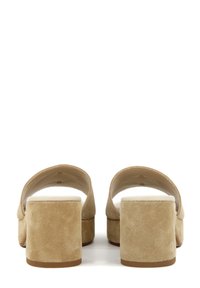 Mule in suede beige con tacco a blocco, aperte sul retro, punta tonda e soletta bianca liscia. L'altezza del tacco è di circa 5 cm.