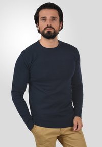 Marineblauer Rundhalspullover aus strukturiertem Strick, hergestellt aus weichem Material, mit langen Ärmeln sowie gerippten Bündchen und Saum.
