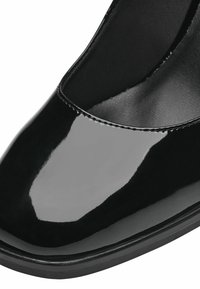 Lesklé černé lakované baleríny s kulatou špičkou, viditelným prošíváním a polstrovaným černým interiérem.