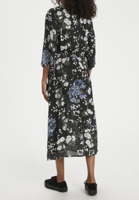 Robe midi florale noire avec des fleurs bleues et blanches, manches longues, taille froncée et silhouette fluide. Assortie avec des baskets noires.