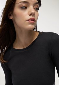 Czarna bluzka z długim rękawem, okrągłym dekoltem, wykonana z gładkiego materiału, o dopasowanym kroju i minimalnych detalach przeszyć.