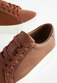 Brune lædersneakers med hvide gummisåler, som har tonede snørebånd, runde snørehuller og en glat overflade. Minimalistisk design.