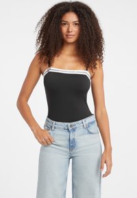 Czarny bodysuit z białymi detalami w postaci pasków oraz logo "Guess Jeans". Połączony z jasnoniebieskimi spodniami typu wide-leg, co podkreśla swobodny styl.