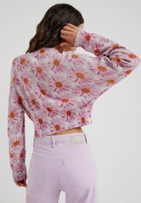 Pull en maille raccourci avec motif marguerite rose et orange ; manches longues et poignets côtelés, associé à un jean lavande clair.