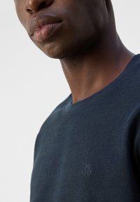 Granatowy sweatshirt wykonany z teksturowanej tkaniny, z okrągłym dekoltem i małym wytłoczonym logo "M OP" na piersi.