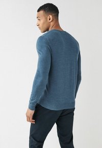 Suéter azul de manga larga en tejido de punto fino, con cuello redondo y puños acanalados. Lleva puesto con pantalones oscuros y ajustados. Textura suave.