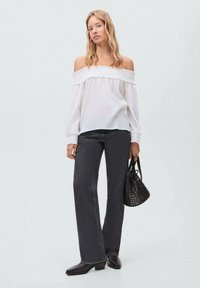 Vit off-shoulder-blus med rynkad halsringning, i kombination med högmidjade svarta jeans. Accessoarer med en liten svart nitas handväska.