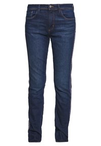 Tmavě modré džíny s úzkým střihem, svislé pruhy v červené, bílé a modré barvě podél boků a tradičním designem pěti kapes.