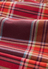 Bawełniana tkanina w czerwoną, pomarańczową i zieloną kratę. Charakteryzuje się teksturowanymi splotami oraz kontrastującymi cienkimi i grubymi liniami.